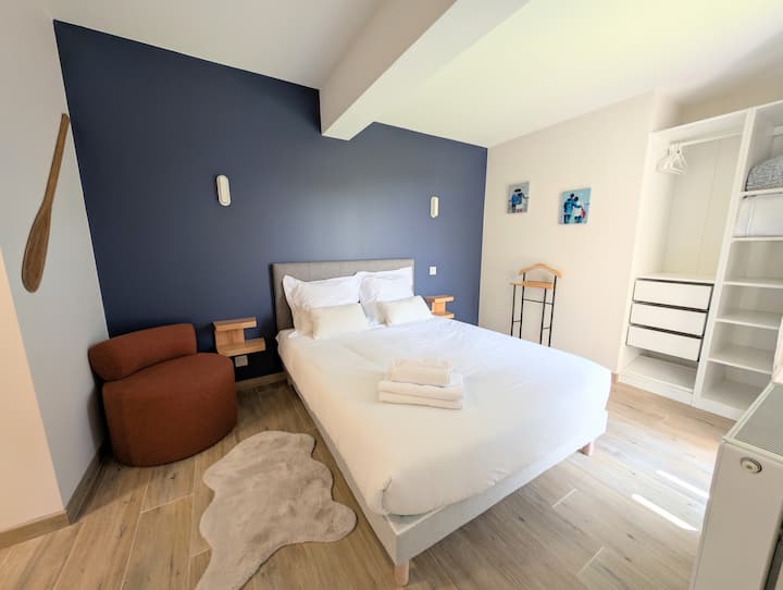 La chambre est décorée dans des tons neutres avec un grand mur bleu foncé derrière le lit double, créant une ambiance apaisante. Un fauteuil et un tapis en fausse fourrure ajoutent une touche de confort.
Draps et serviettes disponibles à la location.