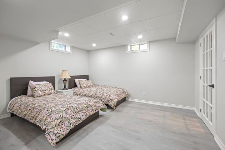 Пространа спална соба на пониско ниво со два двокреветни кревета, светло вдлабнато осветлување и удобна цветна постелнина. Се одликува со ламиниран под, свежи бели ѕидови и влез во француската врата - совршен за деца, пријатели или дополнителни гости кои бараат тивок и мирен престој.