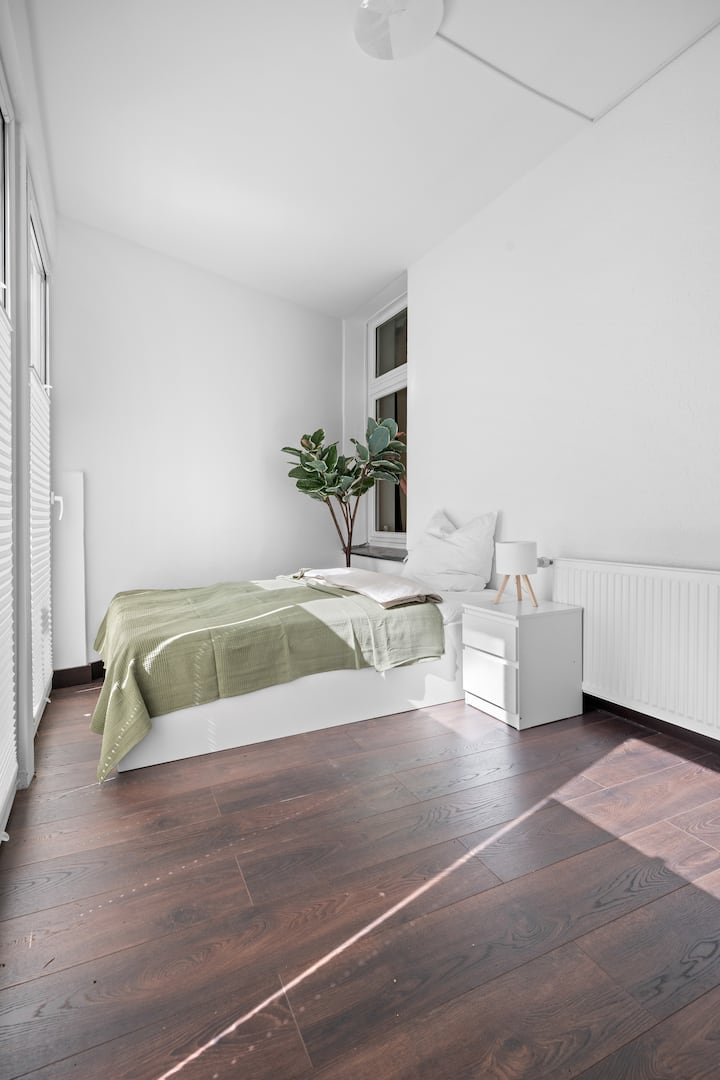 Helles Schlafzimmer mit gemütlichem Bett und beruhigender Atmosphäre. Ideal zum Entspannen – schlicht, modern und mit natürlichen Akzenten eingerichtet.