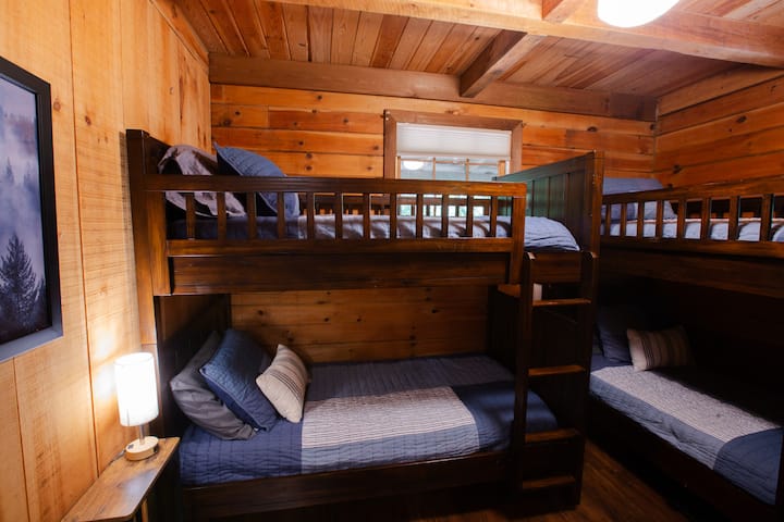 ห้องนอนสองชั้นที่อบอุ่นและน่าอยู่พร้อมเตียงแฝด 4 เตียง เหมาะสำหรับเพื่อน ลูกพี่ลูกน้อง หรือการพูดคุยยามดึก ตั้งอยู่บนชั้นหลัก