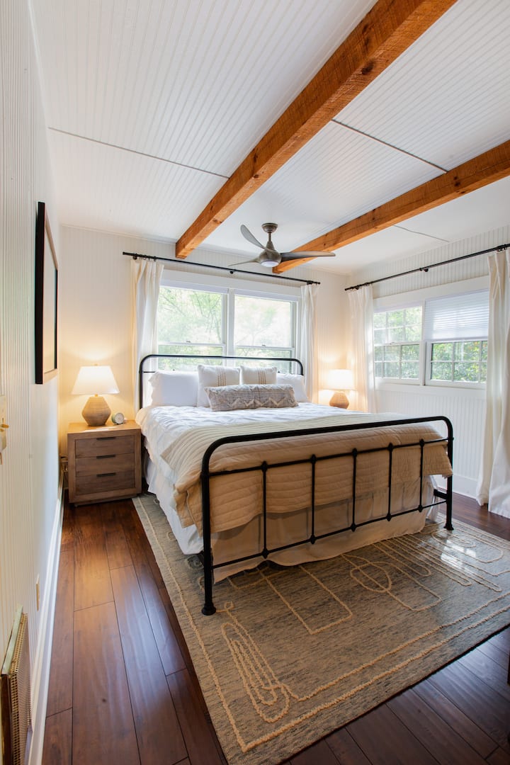 ตื่นมาพร้อมแสงอาทิตย์ยามเช้าที่นุ่มนวลในห้องนอนขนาดคิงไซส์ที่อบอุ่นพร้อมคานสไตล์ชนบทและวิวป่าไม้ ทีวีรุ่น Roku ขนาด 32" วางอยู่เหนือตู้เสื้อผ้าตรงข้ามเตียง มีชั้นวางสัมภาระอยู่ใต้เตียงเพื่อความสะดวกสบายของคุณ ตั้งอยู่ชั้นบน