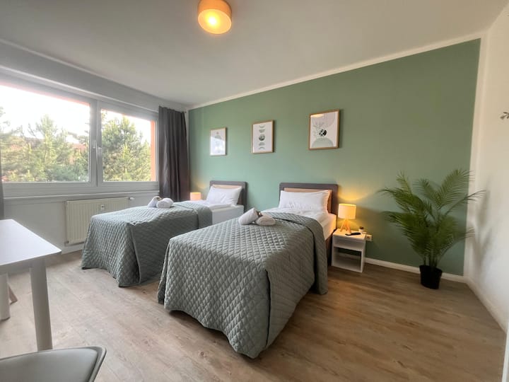 Dhomë gjumi me dy krevate tekë që mund të bashkohen për të formuar një krevat dopio. Përfshin një televizor inteligjent rrotullues, gardërobë të hapur dhe një tavolinë që mund të përdoret si zonë ngrënieje ose hapësirë pune.