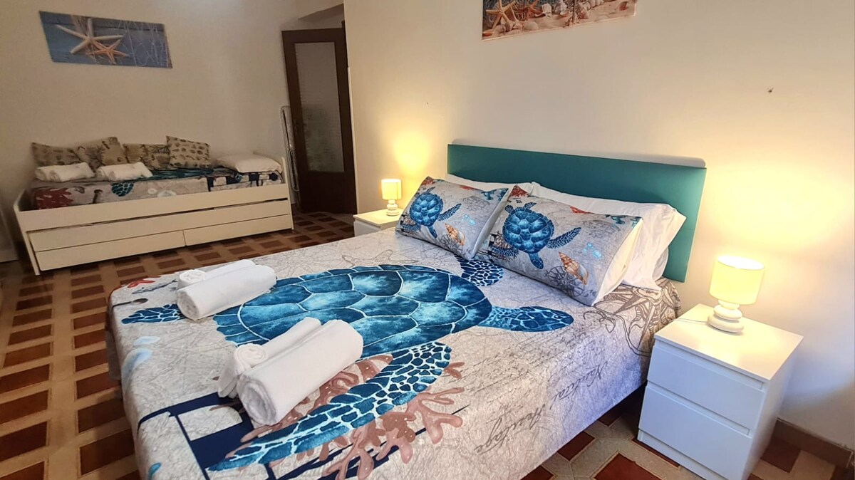 A spacious bedroom features a large bed adorned with a colorful turtle-themed bedspread. A pull-out sofa bed is visible in the background, providing additional sleeping arrangements. Soft lighting from bedside lamps creates a welcoming ambiance.