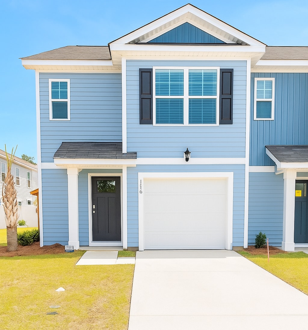 The exterior of a two-story blue home is shown, featuring crisp white trim and a large garage door. Symmetrical windows provide natural light, while a neatly maintained lawn and a small shrub enhance the inviting entrance.