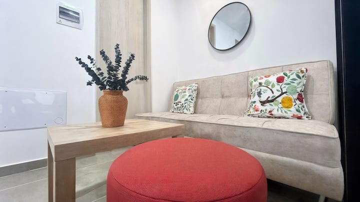 Sala con sofá recto beige, cojines florales y mesa de centro con jarrón.

