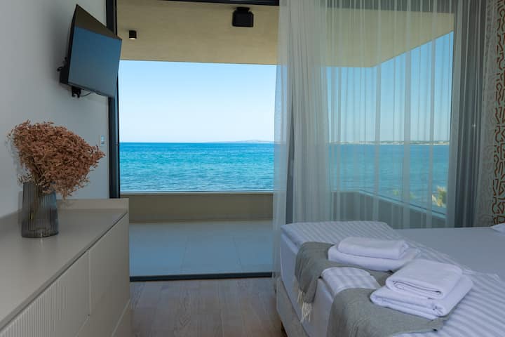 Spacious bedroom with an extra-large double bed, high-comfort mattress, cozy lighting, a dressing table, private bathroom, wardrobe, and direct access to a balcony with a stunning sea view – perfect for peaceful moments.