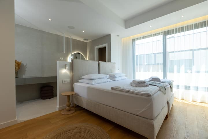Spacious bedroom with an extra-large double bed, high-comfort mattress, cozy lighting, a dressing table, private bathroom, wardrobe, and direct access to a balcony with a stunning sea view – perfect for peaceful moments.