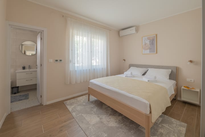 Спална соба 2 со брачен кревет (широк 150-179 см), вклучена е постелнина. Поглед кон градината. Москито мрежи на прозорците. Приватна бања со тоалет и туш. Клима уредот е достапен во оваа соба + голема гардероба.