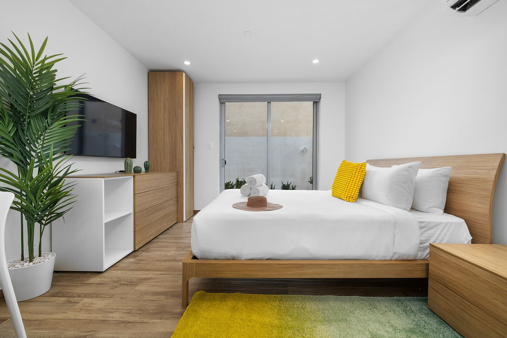 Relájate en una cómoda cama blanca, disfrutando de la luz solar natural y las vistas verdes, todo mientras disfrutas de tus programas favoritos en la televisión.