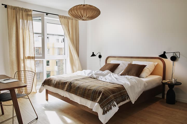 Priestranná spálňa s manželskou posteľou veľkosti King, štýlovým dizajnom a pracovným priestorom pri okne – ideálna na pokojné noci a produktívne chvíle.