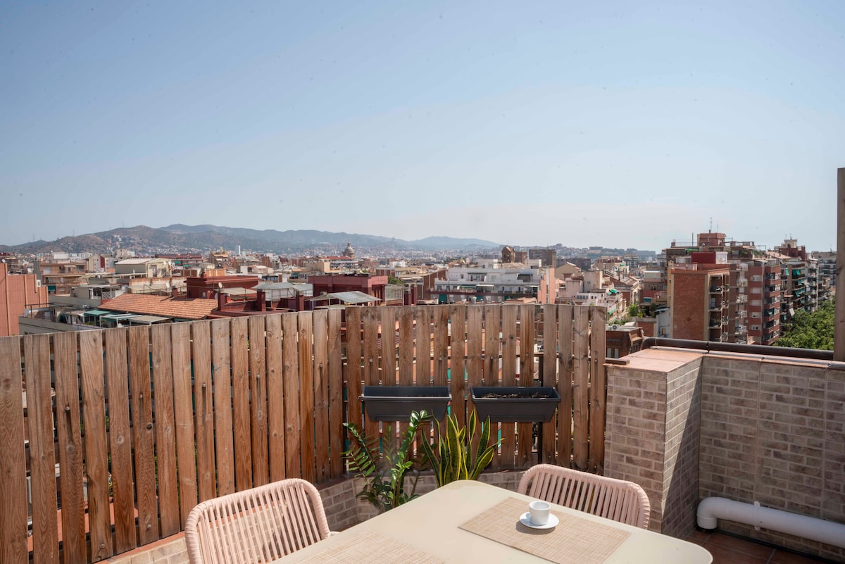A rooftop terrace is depicted, featuring a wooden railing and a table set for two with a cup placed prominently. Views of the cityscape and distant mountains provide a scenic backdrop, while lush greenery adds a touch of nature to the space.