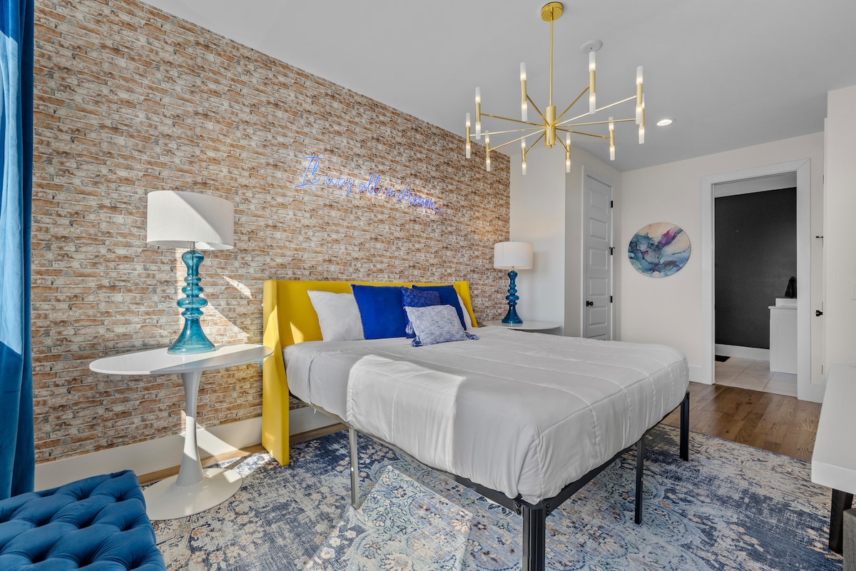 Chumba cha kulala chenye mtindo wa matofali yaliyo wazi, taa za kisasa na rangi kali. Pumzika chini ya alama ya neon na ufurahie mapumziko ya starehe na yenye uchangamfu.