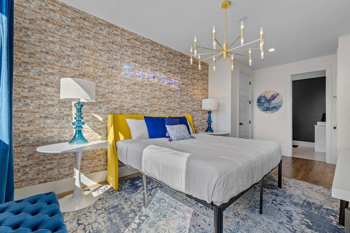 Stylish bedroom with exposed brick, modern lighting, and bold pops of color. Relax under the neon sign and enjoy a cozy, vibrant retreat.