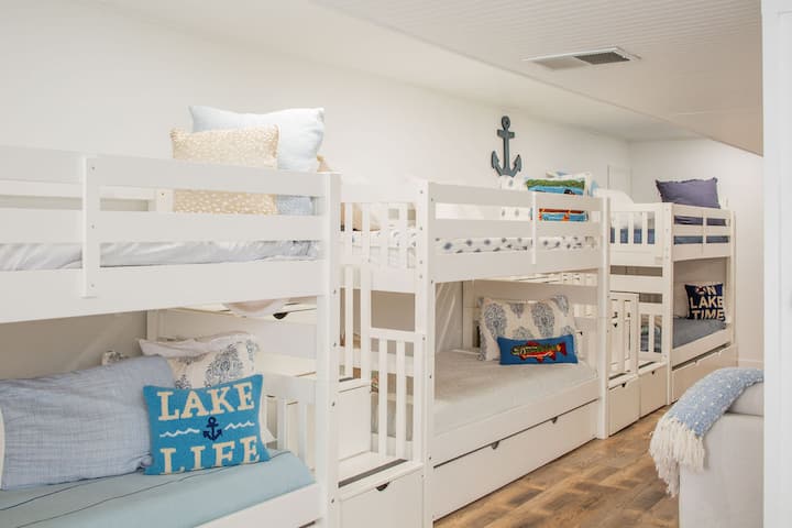 Designed to sleep up to 11 guests, this spacious bunk house features three bunk beds with trundles and one sleeper sofa. It includes an ensuite bathroom with a shower and offers direct access to the lawn through charming French doors.