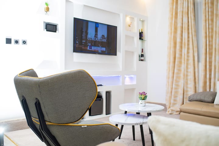 Модерен салон со удобен фотелја, телевизор со рамен екран со DSTV, шик централна маса, удобен кауч, полица за вино и топло осветлување. Елегантните завеси и чистиот под го комплетираат овој светол и привлечен простор совршен за опуштање или забава.