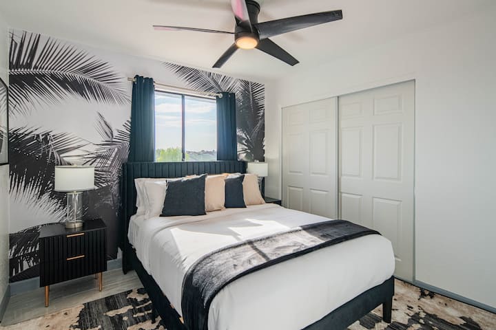 Táto štýlová izba na poschodí má pohodlnú manželskú posteľ, odvážnu stenu s palmovými vzormi a moderné čierne a neutrálne detaily, ktoré vytvárajú elegantnú a uvoľnenú atmosféru.