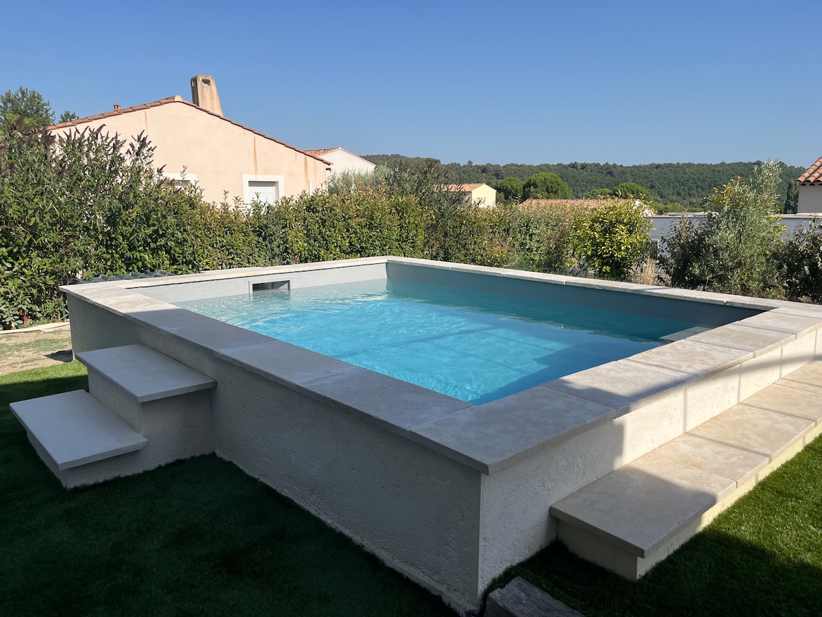 The image features a modern pool surrounded by a stone terrace, situated in a serene outdoor setting. Steps lead into the clear water, and lush greenery borders the area, providing a private ambiance. Soft sunlight reflects off the water's surface, enhancing the tranquil environment.