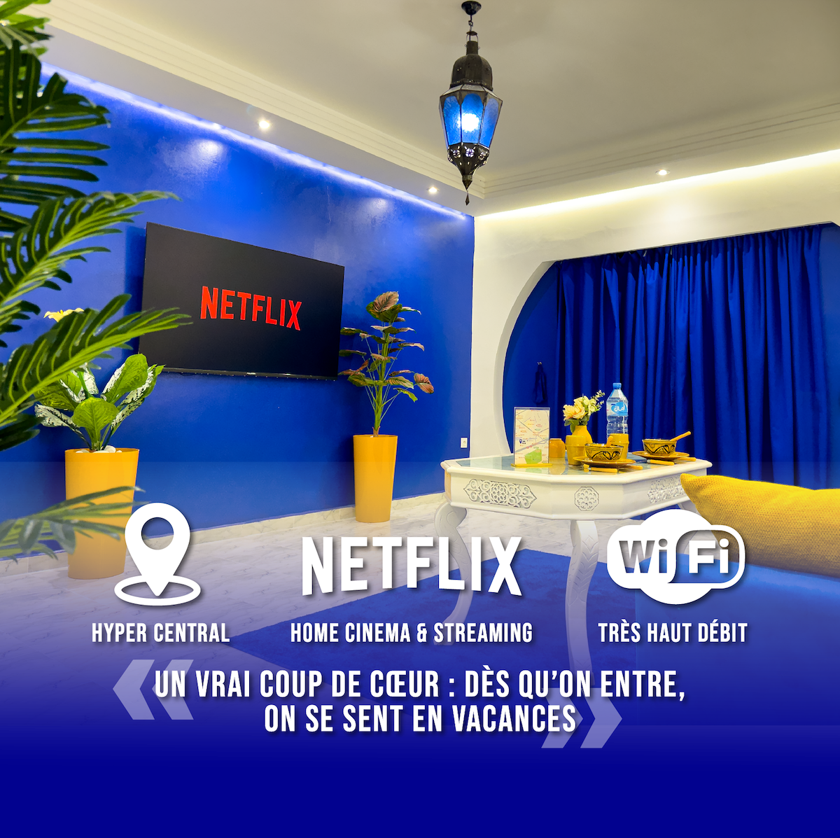 A cozy corner of the living area is highlighted by a flat-screen TV displaying the Netflix logo. Blue curtains frame the scene, complemented by decorative plants. A low table with refreshments is placed in front, creating an inviting atmosphere for relaxation and entertainment. Wi-Fi connectivity is indicated prominently.