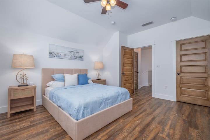 Quaint queen bedroom located upstairs. Features a luxury mattress and bedding, plenty of storage, a suitcase rack, and a closet.