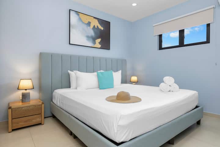 Განიტვირთეთ ნათელი, ფართო საძინებელში კომფორტული საწოლებით, ახალი თეთრეულით, კედლის მინიმალისტური ხელოვნებითა და თბილი განათებით ორი გვერდითი მაგიდის ლამპიდან.