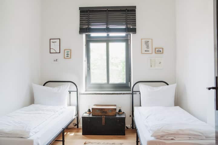 חדר שינה קטן עם 2 מיטות יחיד המשקיף על הגינה ועל הכבשים שלנו