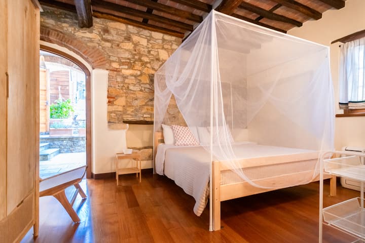 Cama tamaño king con mosquitera y marco, baño privado con ducha, armario, silla, mesitas de noche, lámpara, espejo de cuerpo entero, puerta privada a la terraza exterior.
