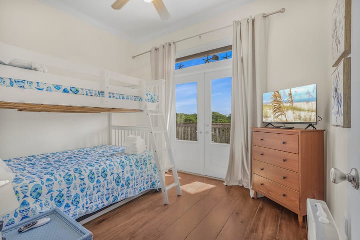A cheerful bunk room made for memories, perfect for kids or friends to relax, watch a movie, and wake up to sunshine streaming through the doors.