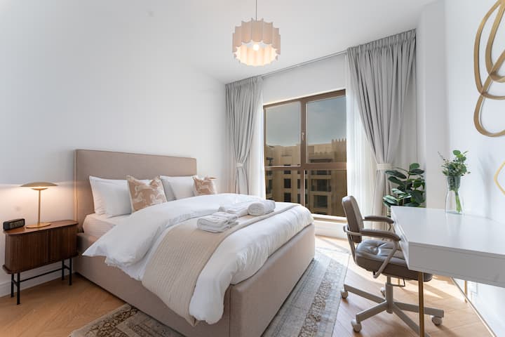 ห้องนอนกว้างขวางพร้อมเตียงหรูหรา แสงไฟสีอ่อน ตู้เสื้อผ้าในตัว และหน้าต่างบานใหญ่ที่เปิดรับแสงธรรมชาติและมองเห็นวิวที่เงียบสงบ