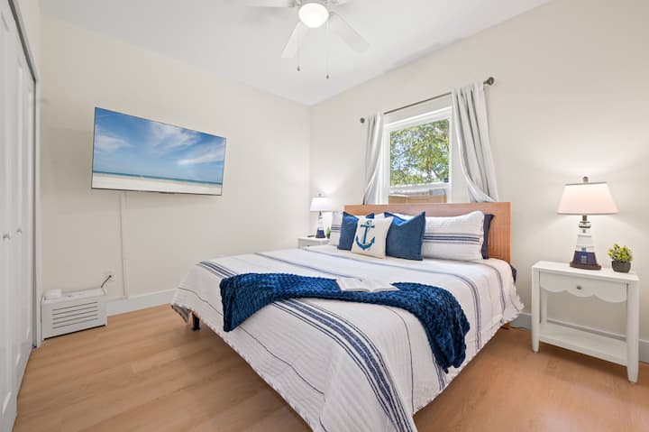 Spavaća soba s bračnim krevetom i pomičnim televizorom od 55", osnovnim sadržajima za vježbanje (utezi + prostirka), opremom za glačanje i detaljima prikladnim za obitelj, uključujući stolicu za hranjenje i ogradicu za igru.