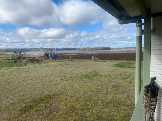 A view from the verandah showcases a rural landscape with a mix of grassy land and cultivated fields. In the distance, a wooden structure is visible near the farm dam, with expansive clouds spreading across the blue sky.