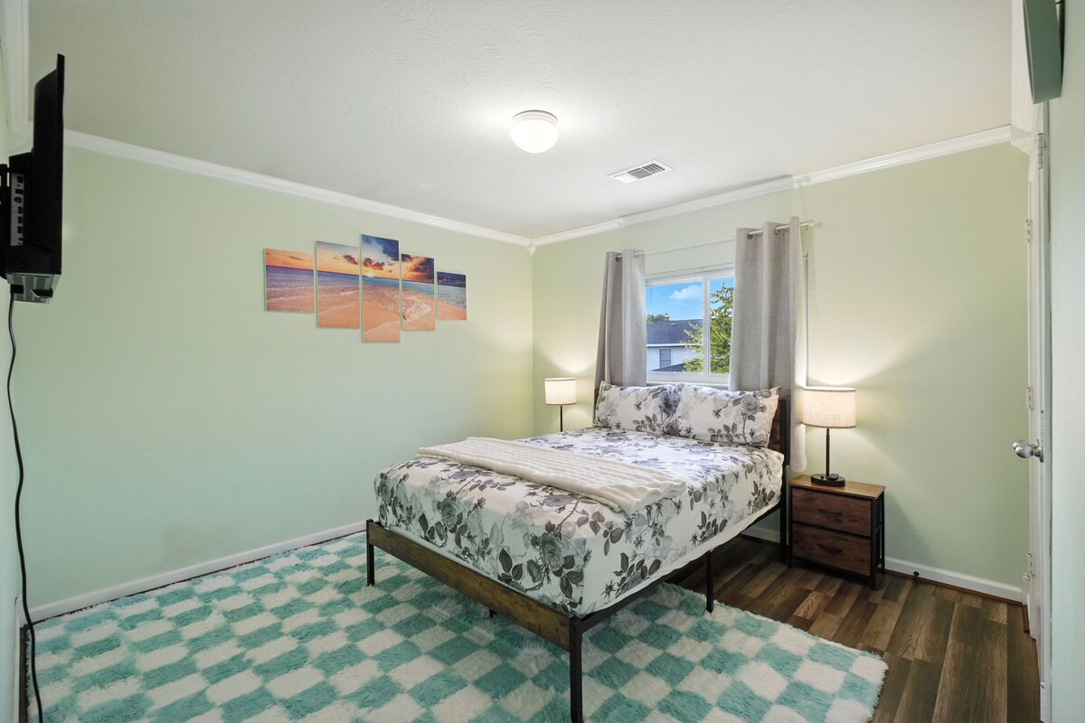 חדר שינה מואר עם מיטת קווין סייז, טלוויזיה, ארון, שטיח רך ואור חלון לנוחות