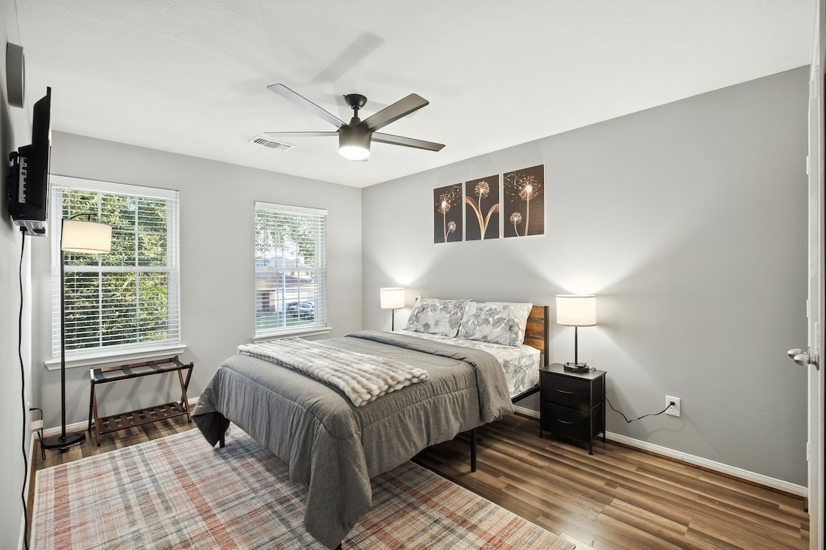 חדר שינה נעים עם מיטת קווין סייז, טלוויזיה, ארון וחלונות בהירים לאור טבעי