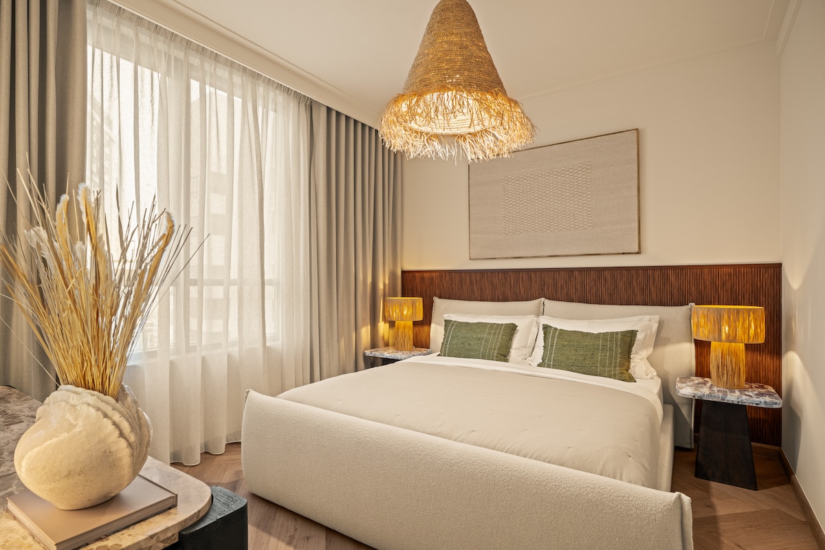 Zobuďte sa v tejto štýlovej a pokojnej spálni s úchvatným výhľadom na panorámu mesta. Izba s oknami od podlahy až po strop, prírodnými textúrami a elegantnou výzdobou kombinuje moderné pohodlie s teplou a príjemnou atmosférou.