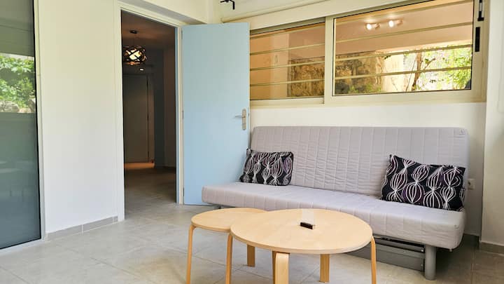 صالة واسعة ومضاءة بالشمس تتميز بسرير أريكة قابل للسحب لاثنين من الضيوف الإضافيين وتلفزيون ذكي 65 بوصة ونوافذ تطل على الحديقة لإقامة مريحة.