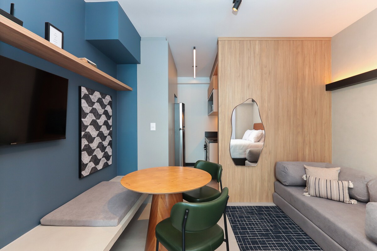 Sala de estar integrada con TV, mesa de comedor con banco + sillas de cuero, sofá cama doble, espejo de cuerpo entero y alfombra