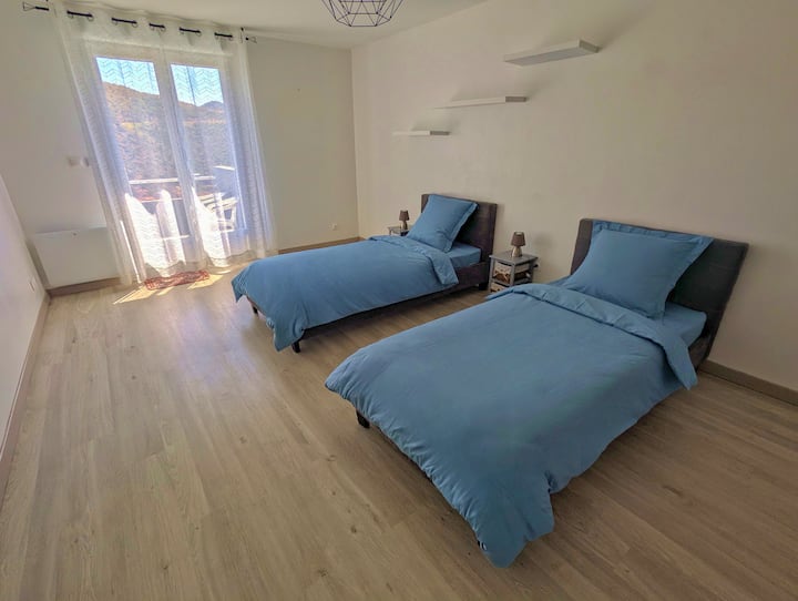 Chambre avec deux lits simples et accès terrasse intermédiaire.