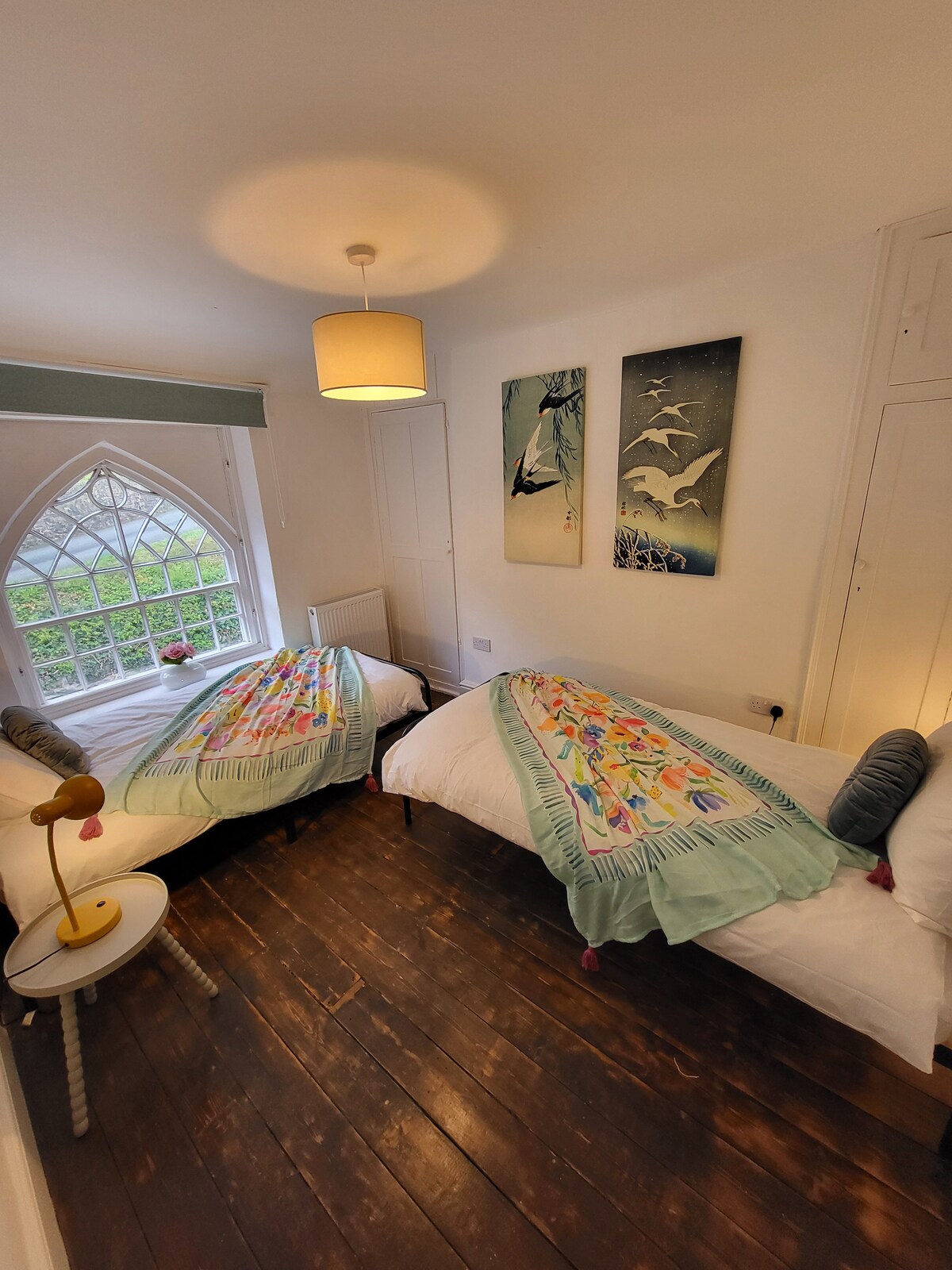 Dhomë gjumi komode me dy krevate tek, ndriçim të butë dhe mbulesa shumëngjyrëshe.