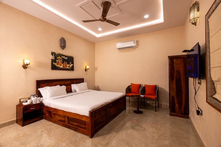 Bedroom 3 – Moti Mahal: Elegant and well-lit, featuring a double bed, AC, ceiling fan, TV, wardrobe, and cozy seating. Beige walls, recessed lighting, and tasteful decor create a refined, comfortable space perfect for relaxation.
