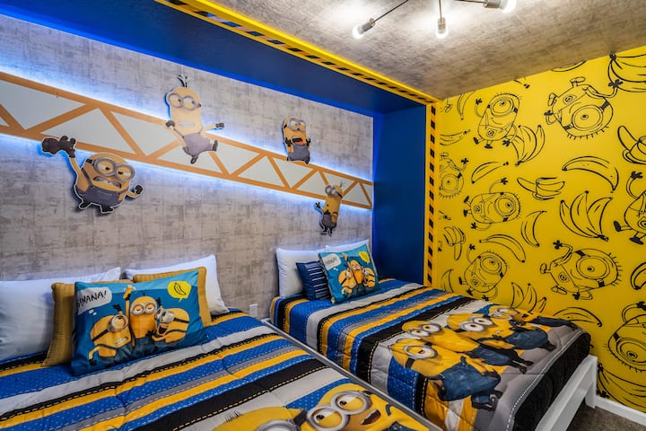 Plongez dans un laboratoire de Minions espiègles : des lits complets à rayures bleues et jaunes audacieuses, un mur décoratif de bananes avec une bordure de mise en garde, et une poutre lumineuse où les petits aides grimpent, où l'heure du coucher se transforme en missions rigolotes et en rêves alimentés par les bananes.         