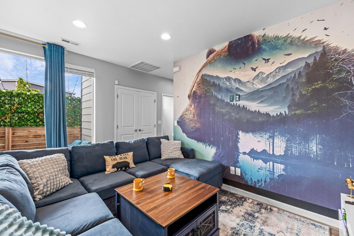 Un televisor de 75 pulgadas con un sistema de sonido de alta calidad y un sofá amplio y cómodo, todo frente a un impresionante mural que captura el espíritu de Colorado.