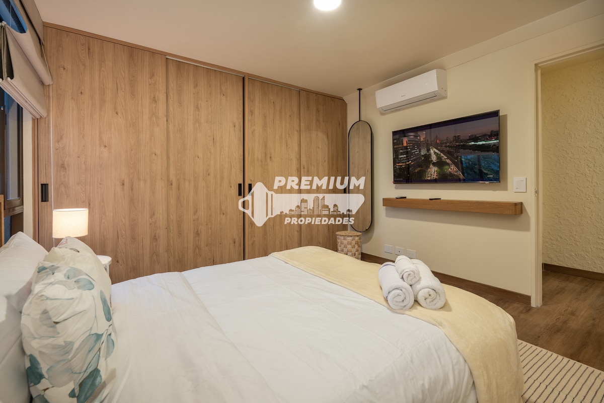 Удобна спалня с двойно легло, меко спално бельо, климатик и телевизор на стената.