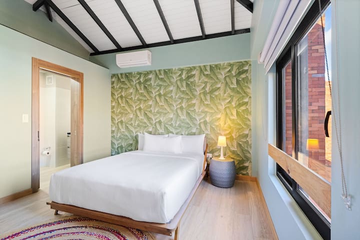 Camera da letto accogliente e luminosa con una parete con motivo a foglie tropicali, un soffitto alto inclinato e un design pulito e moderno.