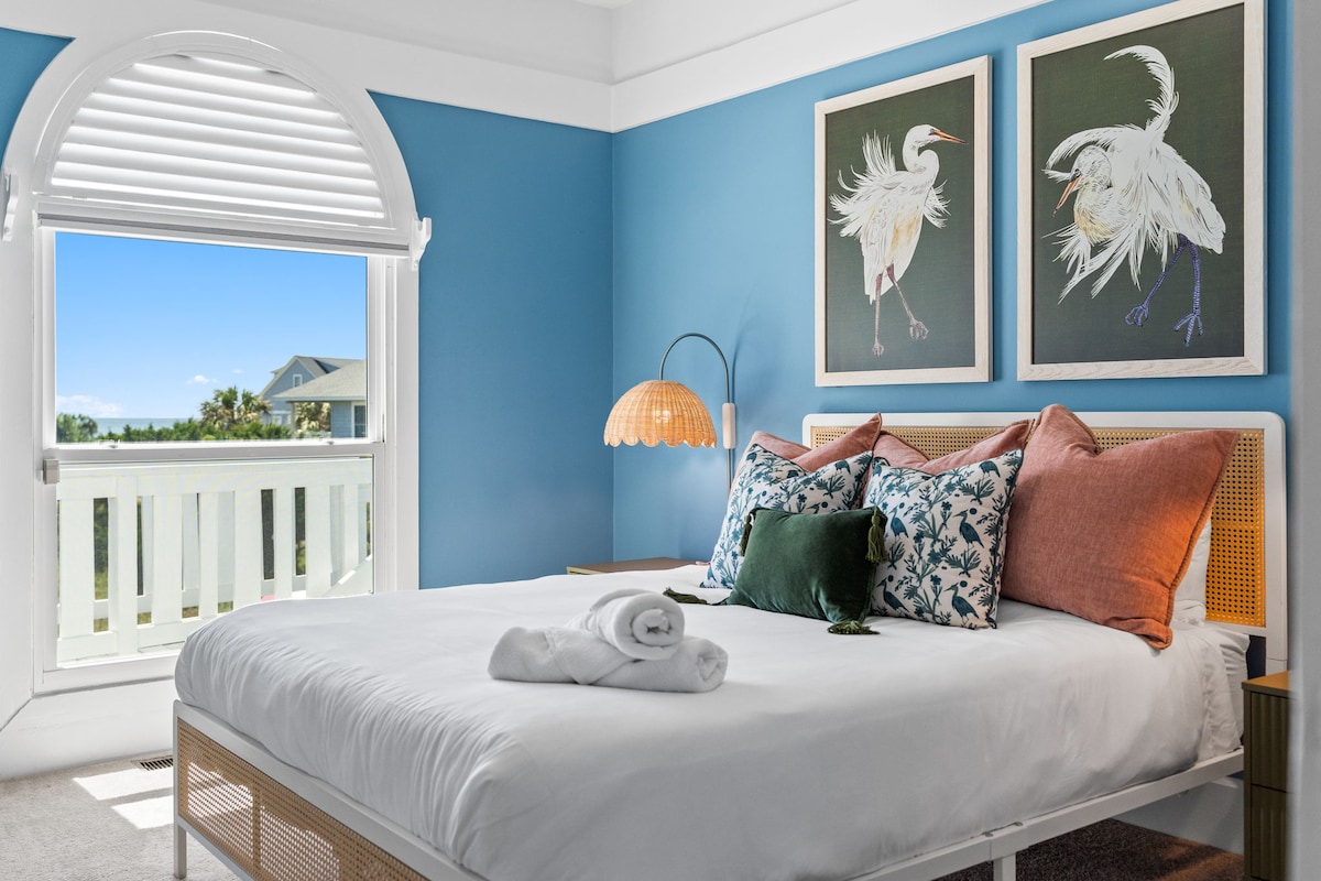 Chumba cha kulala cha kupendeza: Kuta angavu za bluu huweka sehemu ya mapumziko yenye utulivu yenye mandhari nzuri ya ufukweni na mapambo ya kisanii.