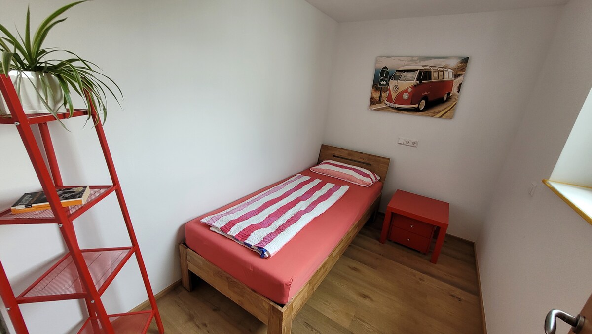 Chumba chetu kidogo zaidi kinaonekana kuwa na rangi nyekundu. Rafu ndogo na pia meza za kando ya kitanda zilizo na droo zinaweza kuwa na vitu vya faragha.