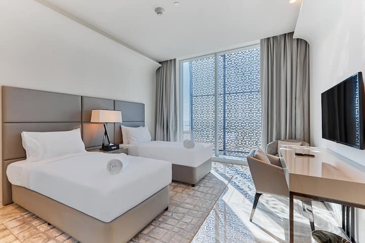 Táto spálňa ponúka dve samostatné postele, televízor a pracovný stôl s pripojenou kúpeľňou s vaňou na oddych.