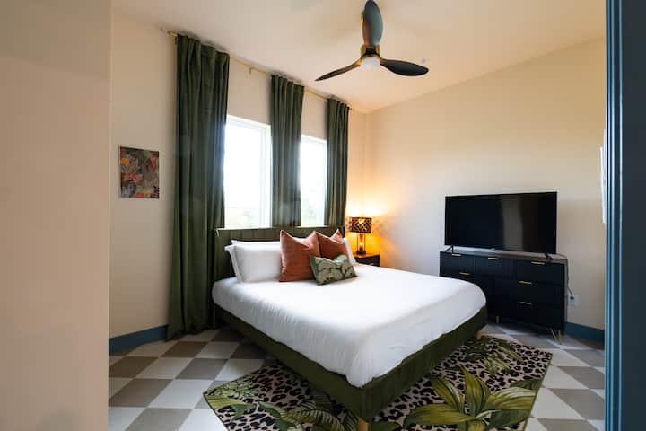 Útulná spálňa s modernou posteľou, zelenými závesmi a televízorom s plochou obrazovkou – ideálna na pohodlie a zábavu.