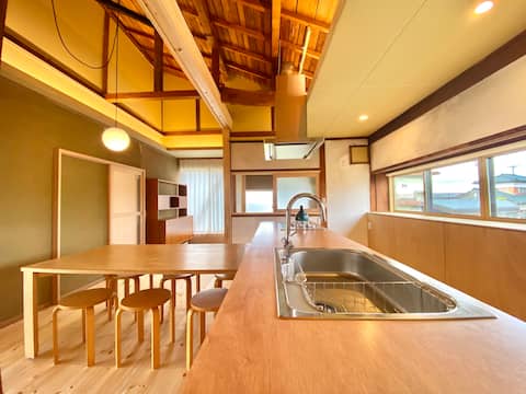 A house with a large veranda, tatami room, and open kitchen with a ceiling fan. The kitchen and bath
