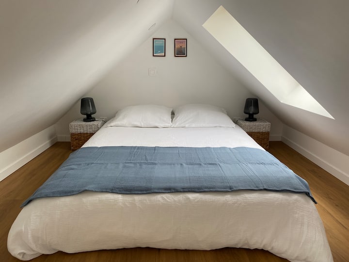 Habitación enclavada bajo techo, accesible por una escalera de molinero con cama elevada y zona de lectura acogedora. 
Almacenamiento inteligente en cestas, perchero, sillón cómodo y tragaluz para un ambiente acogedor de cabaña.