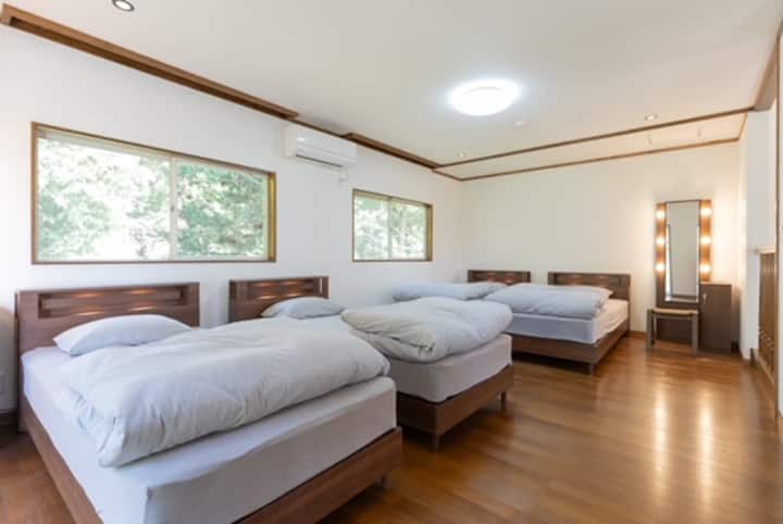 Спална соба со зеленило на дрвја надвор од прозорецот, опкружена со нежен природен поглед.