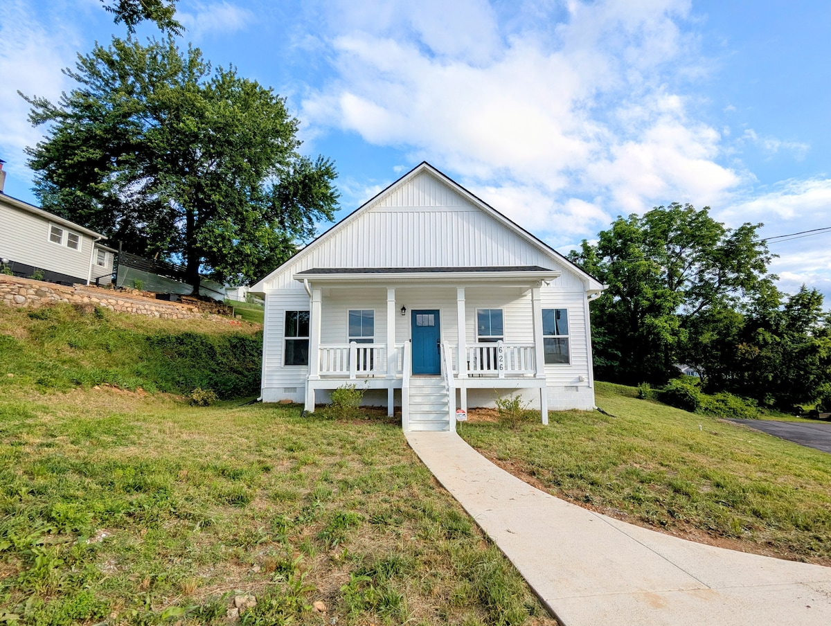 The newly built home is surrounded by a landscaped yard, featuring a pathway leading to the inviting front porch. The exterior is characterized by white siding and a prominent blue door, with large windows allowing natural light into the interior.